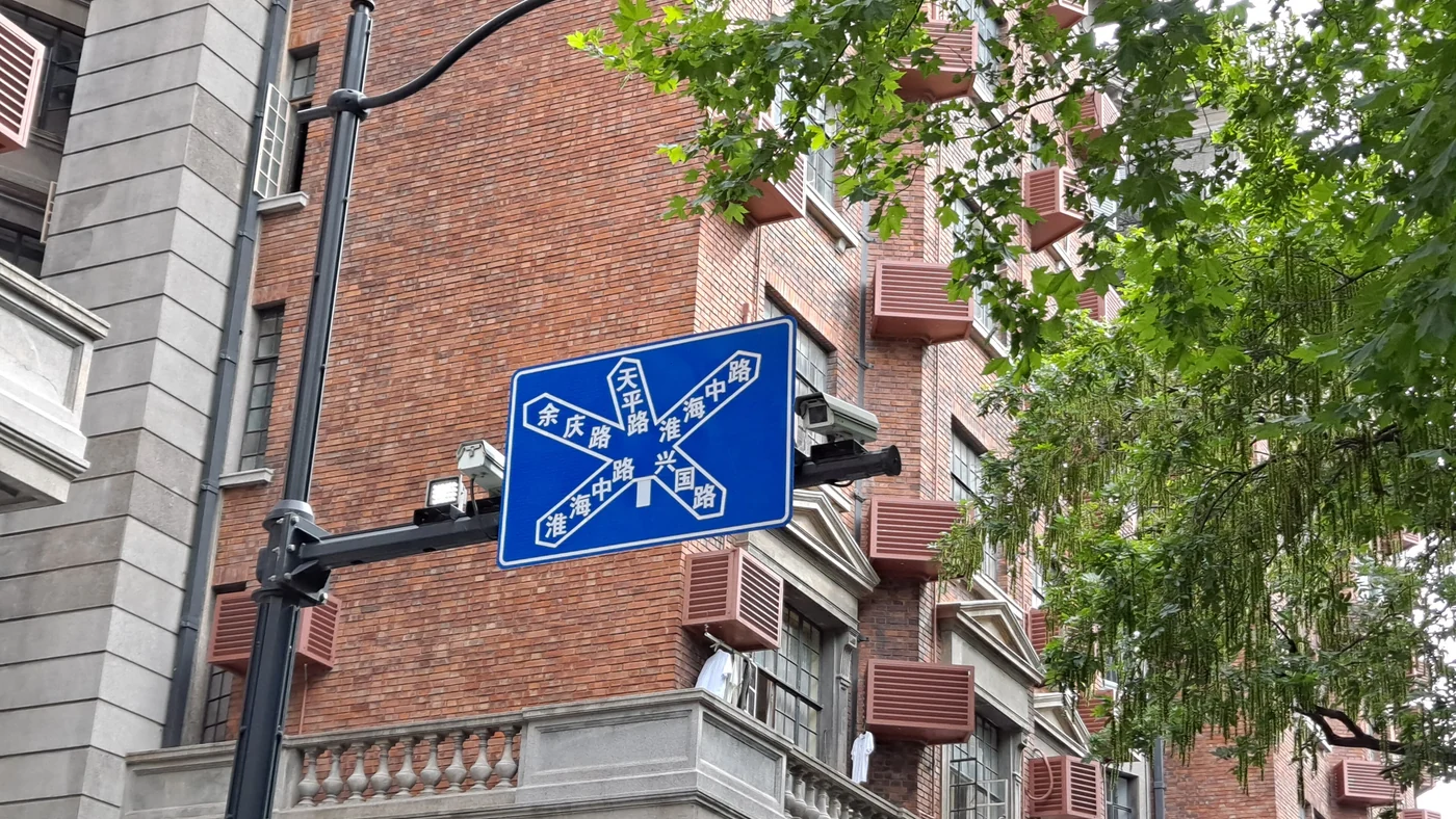 A blue street sign beside brick buildings and green trees at Wukang Road in Shanghai